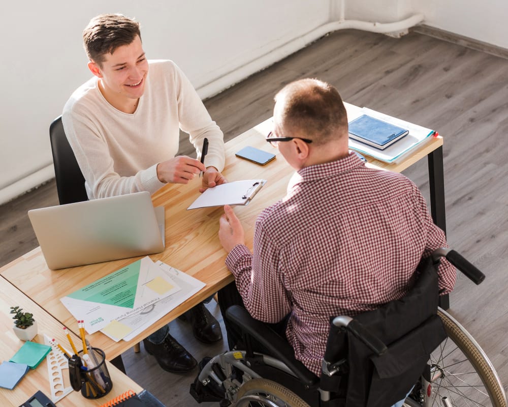 Support worker assisting a young man with disability during an art painting session, promoting NDIS community participation and creative skill development.