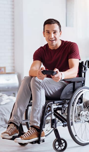 Young man in a wheelchair playing video games at home, highlighting independence and supported independent living under NDIS care services.